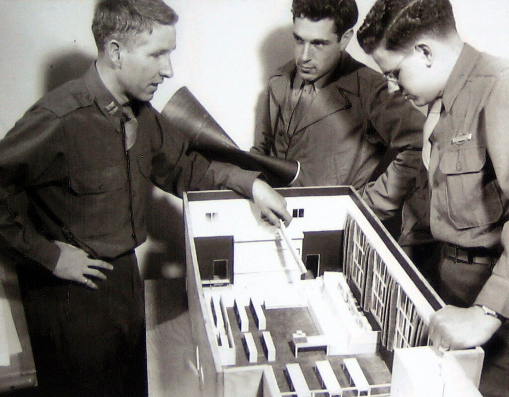 Circa October 1945: L-R Captain Daniel Kiley, Lieutenant James Johnson, and model-builder John Meyerdiscuss the model of redesigned Nuremberg Palace of Justice Courtroom 600.