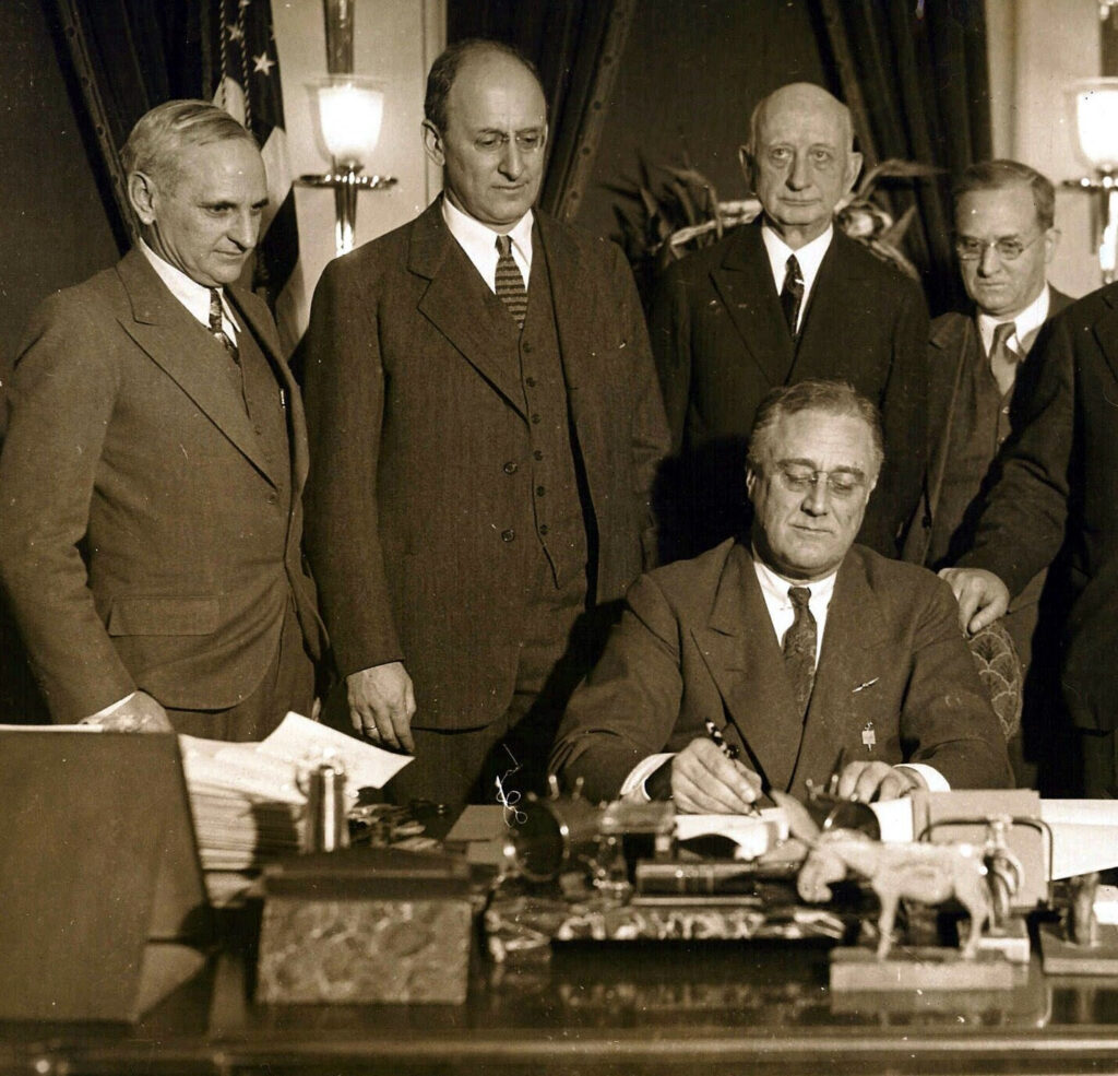 January 30, 1934: President Roosevelt reenacting for cameras his signing of the Gold Clause law. L-R: Treasury Department general counsel Herman Oliphant; Treasury secretary Henry Morgenthau, Jr., Federal Reserve Governor Eugene Black; FDR; and New York Federal Reserve Governor George Harrison.